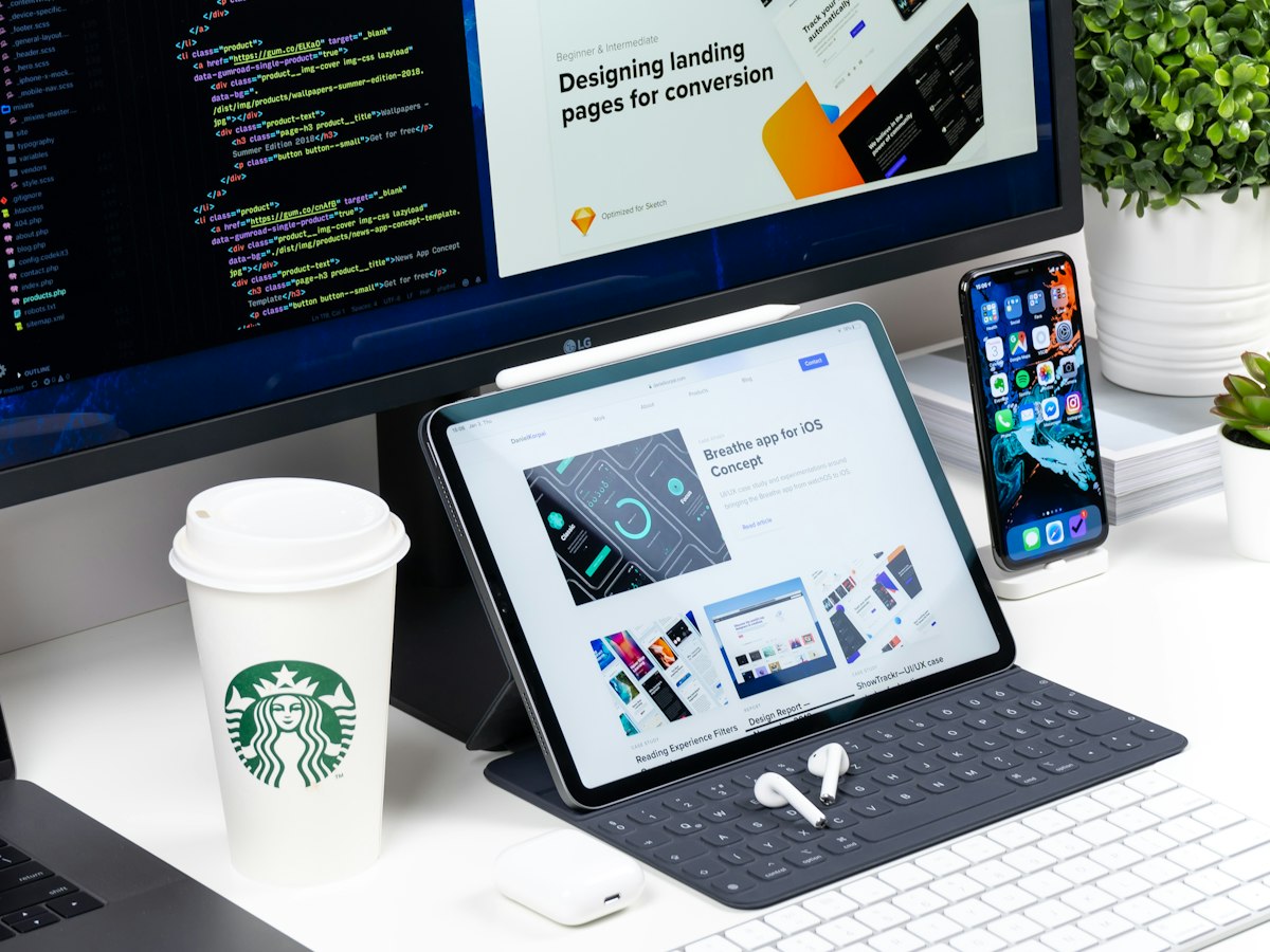 A desk with a monitor showing code beside a tablet and phone displaying web designs